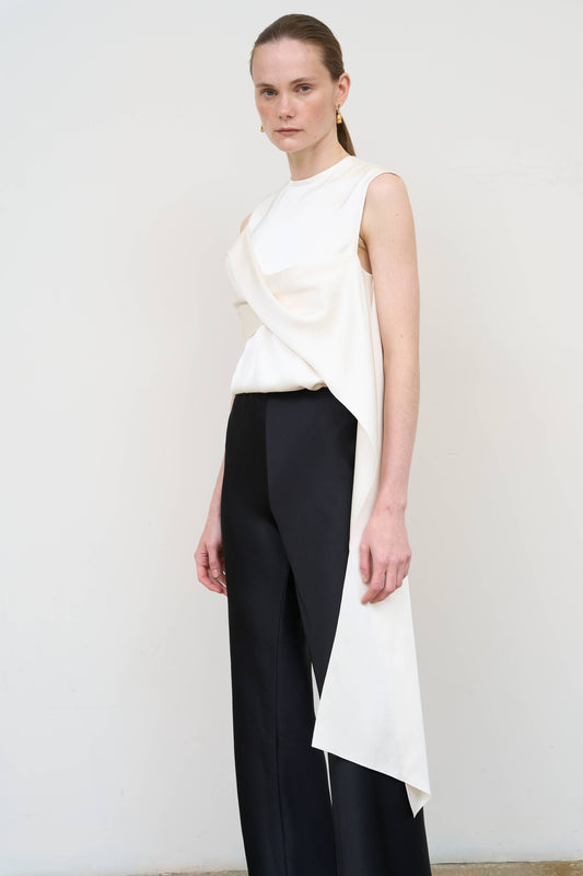 Model is wearing an asymmetric white twist top by Litkovska with sculptural draping and sleeveless design, modern designer top available at House of Woven Stories