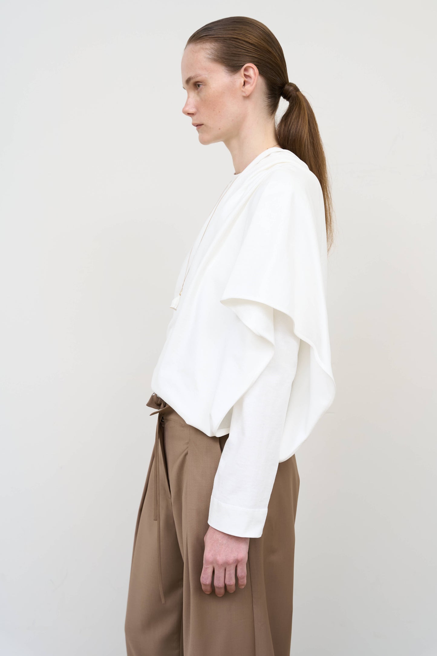 Model is wearing a white asymmetric cotton longsleeve by Litkovska with elongated silhouette and subtle architectural asymmetry, designer women’s top available at House of Woven Stories