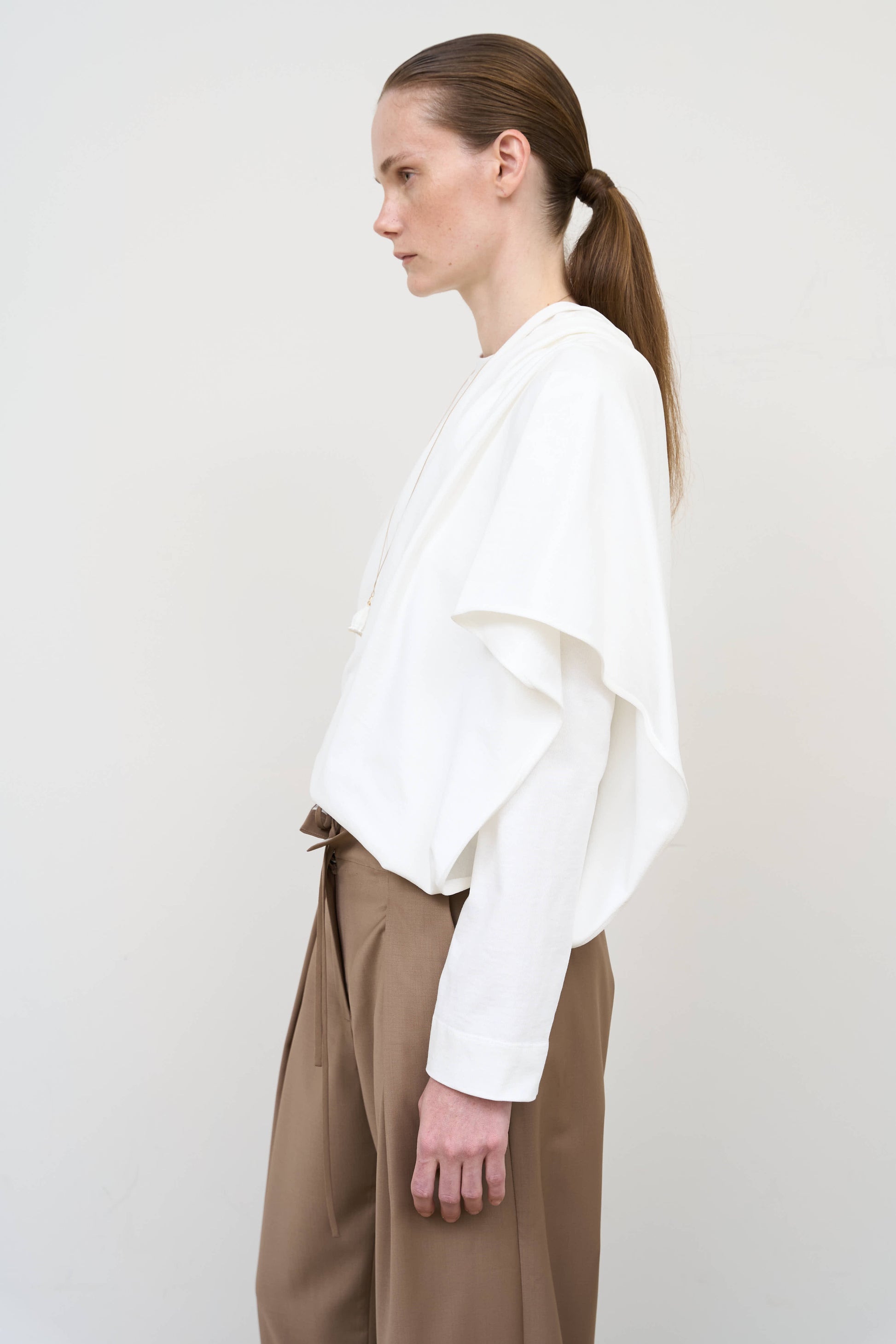 Model is wearing a white asymmetric cotton longsleeve by Litkovska with elongated silhouette and subtle architectural asymmetry, designer women’s top available at House of Woven Stories