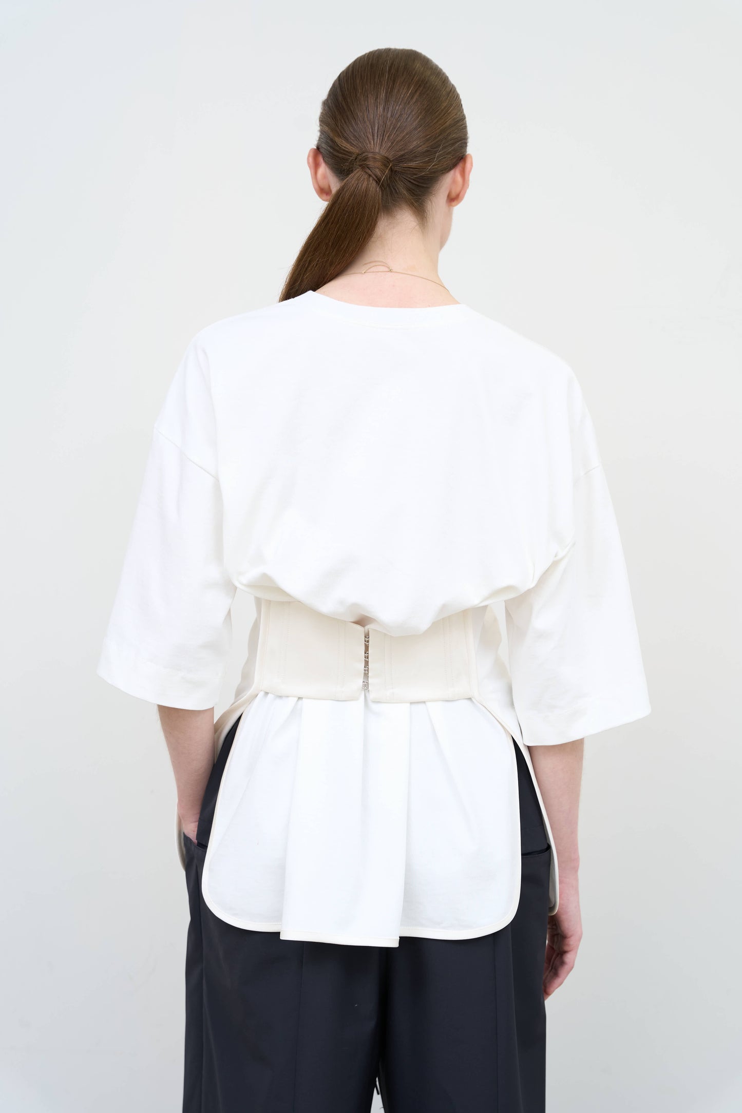 Model is wearing a white Corset T-Shirt by Litkovska with integrated corset-inspired waist panel and relaxed silhouette, designer women’s top available at House of Woven Stories