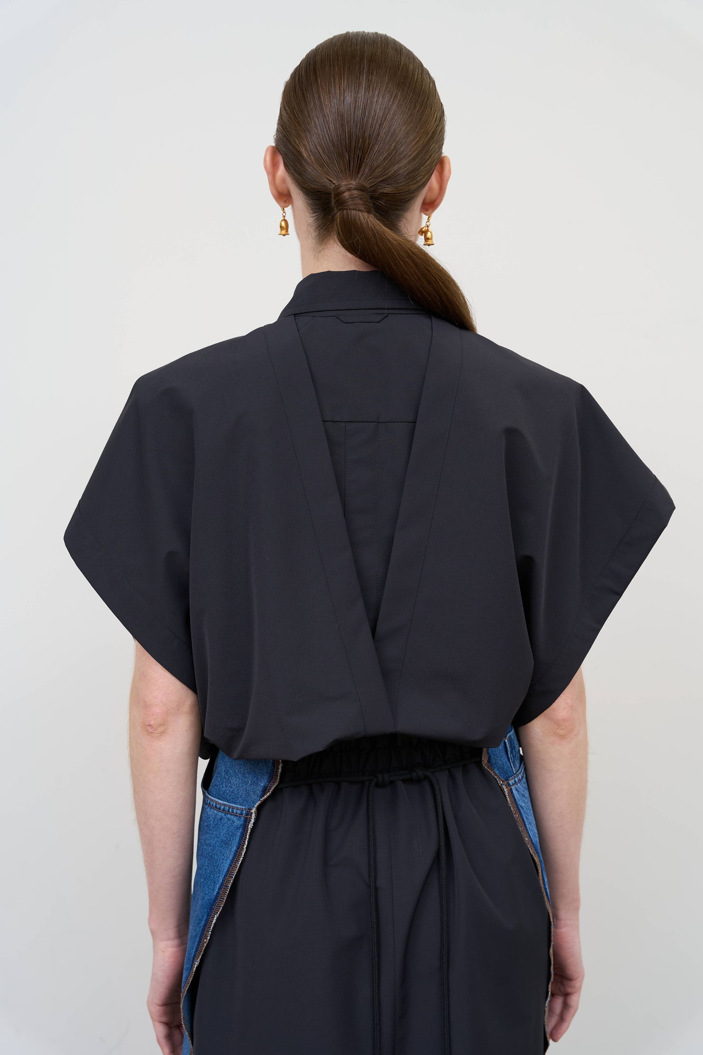 Model is wearing a deconstructed black wool-blend sleeveless shirt by Litkovska with architectural tailoring and elongated silhouette, designer women’s shirt available at House of Woven Stories