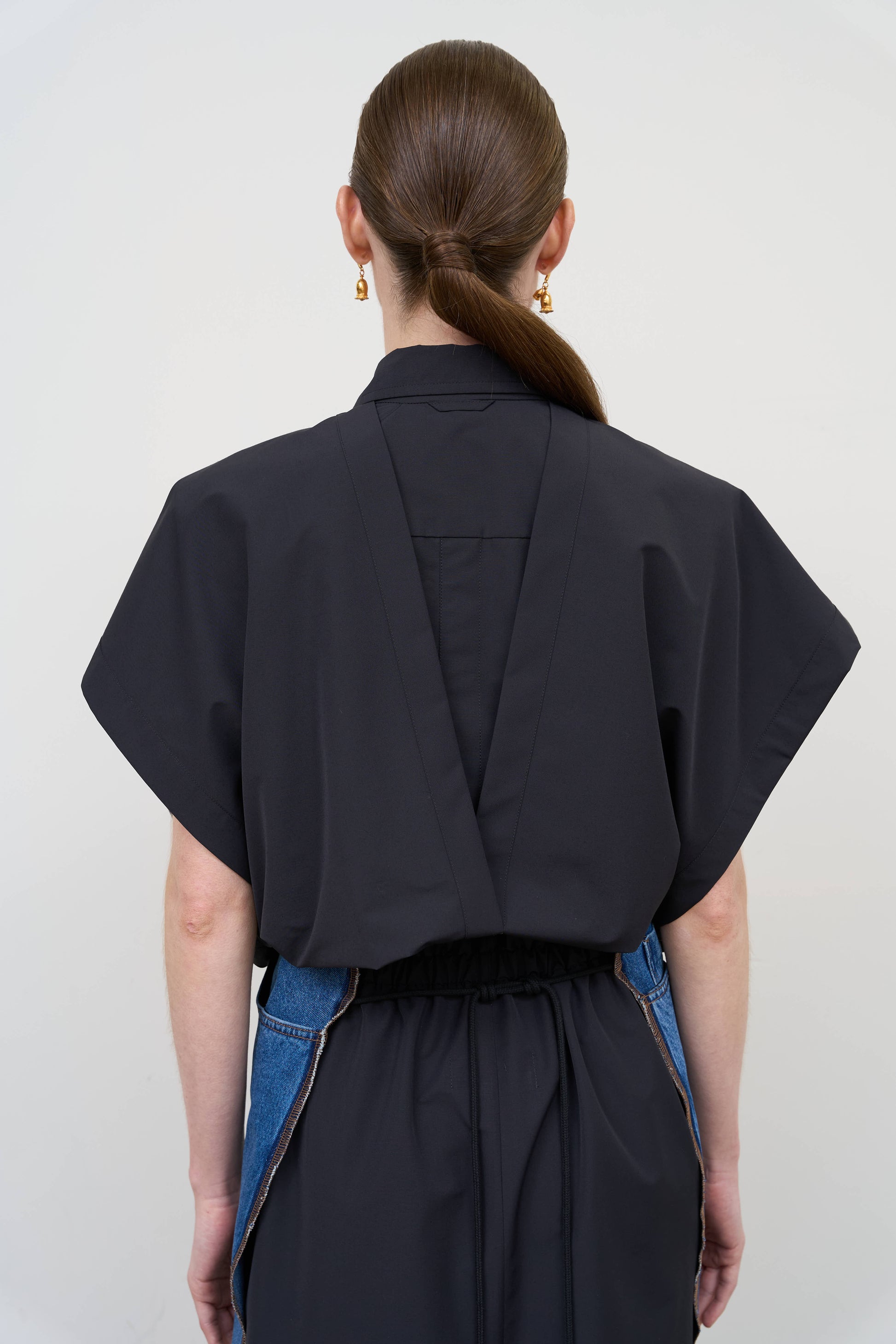 Model is wearing a deconstructed black wool-blend sleeveless shirt by Litkovska with architectural tailoring and elongated silhouette, designer women’s shirt available at House of Woven Stories