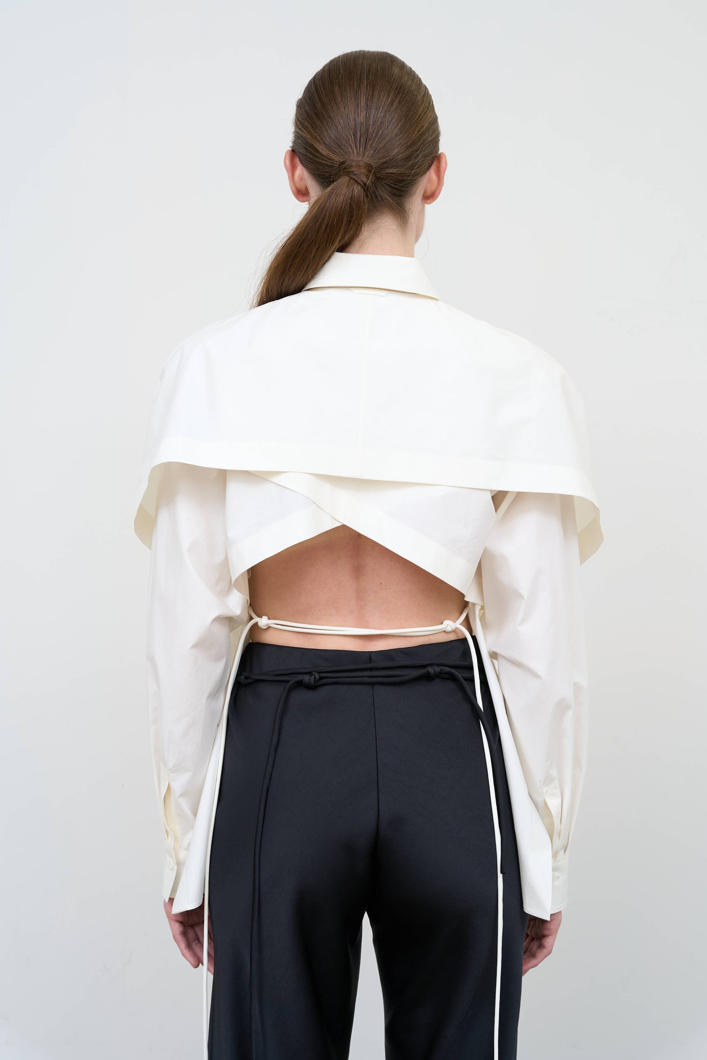 Model is wearing a fitted white cotton shirt by Litkovska with capelet overlay and open-back detail, architectural designer top available at House of Woven Stories