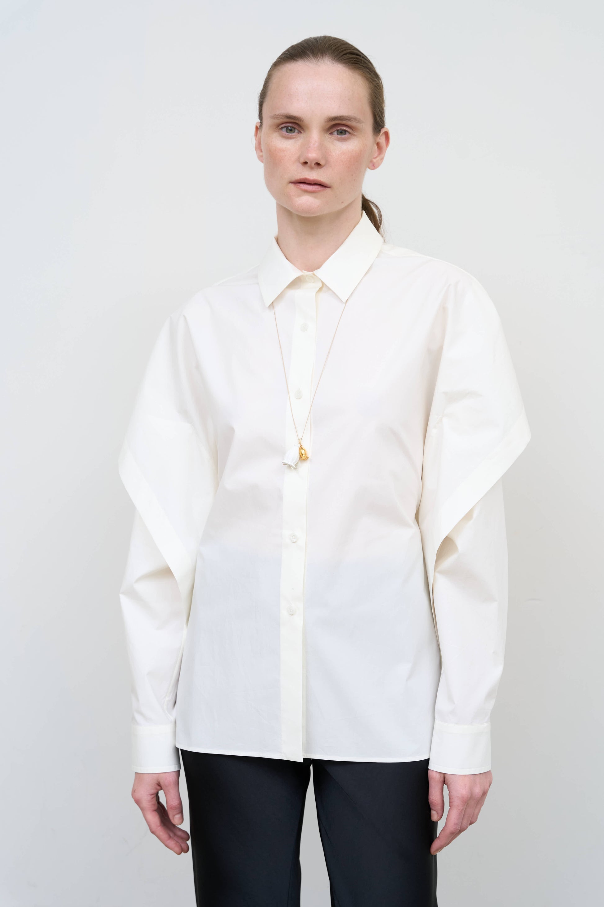 Model is wearing a fitted white cotton shirt by Litkovska with capelet overlay and open-back detail, architectural designer top available at House of Woven Stories