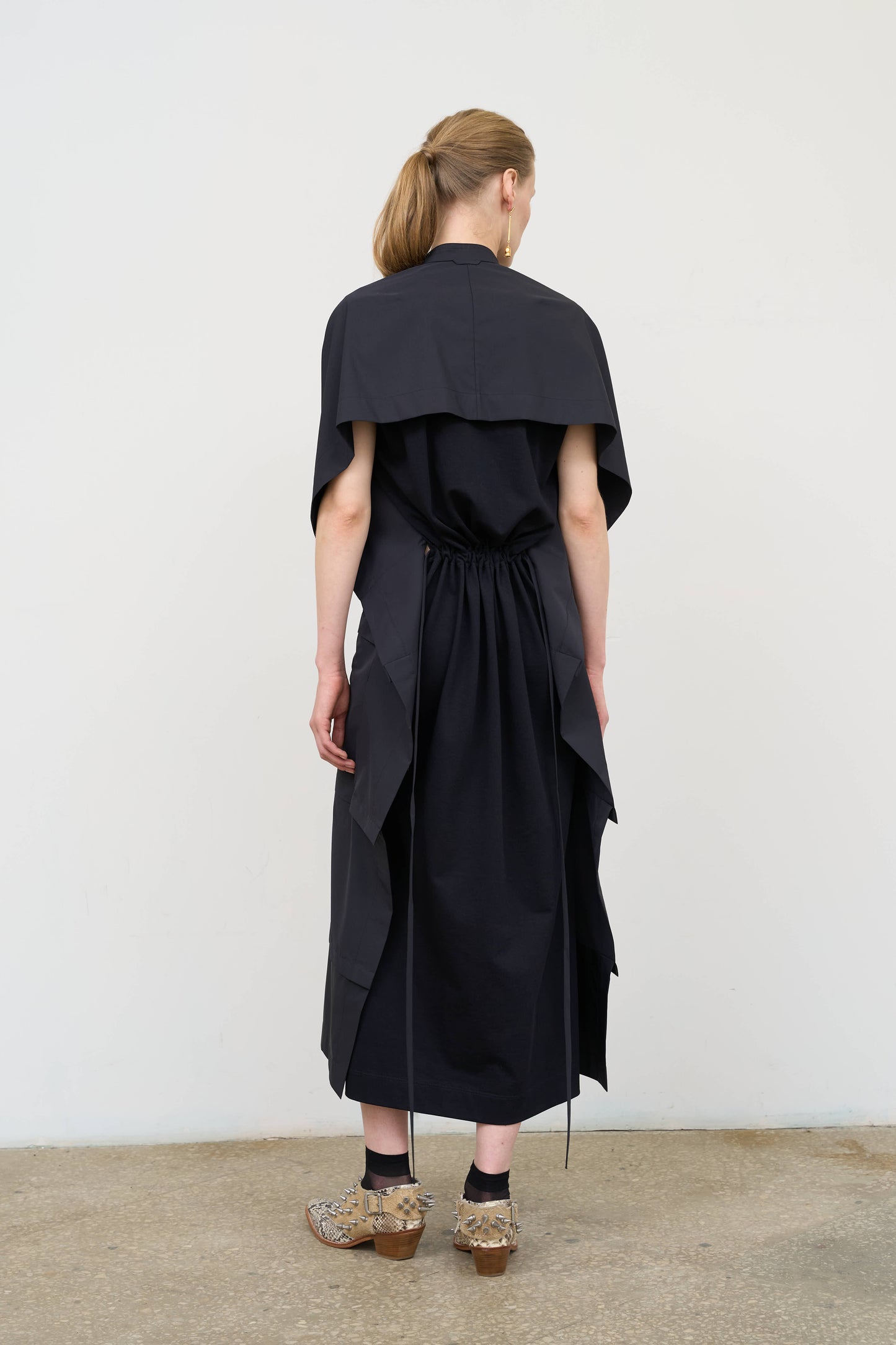 Model is wearing a midi dress by Litkovska with capelet detail, layered wool-blend structure and cotton elements, designer women’s dress available at House of Woven Stories