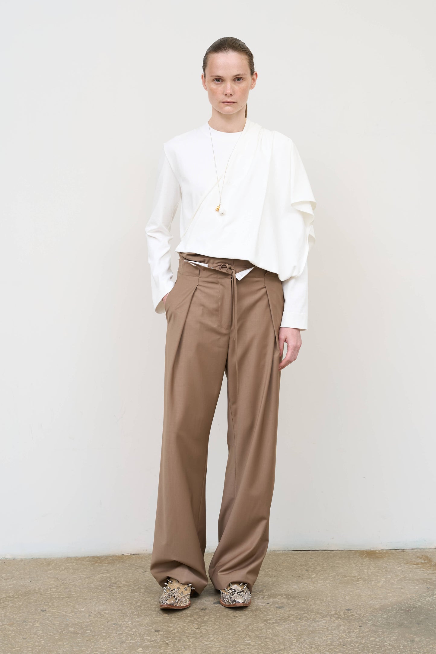 Model is wearing high-rise pleated pants by Litkovska with drawstring waist and relaxed straight leg, designer women’s trousers available at House of Woven Stories