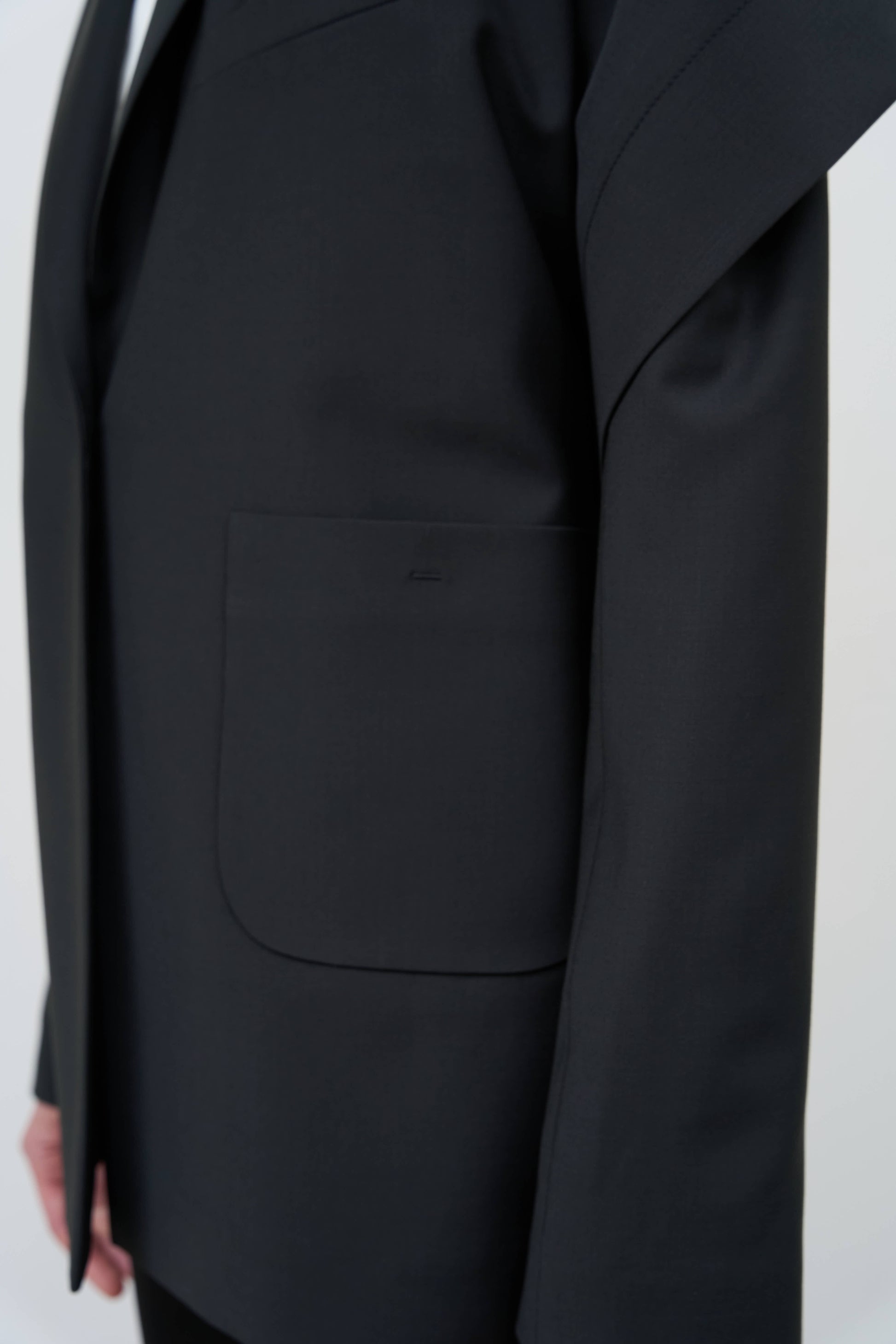 Model is wearing a black tailored wool-blend jacket by Litkovska with capelet overlay and architectural design, designer women’s jacket available at House of Woven Stories