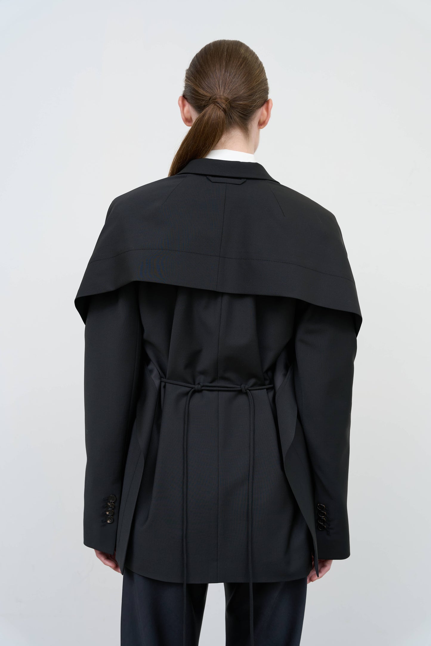 Model is wearing a black tailored wool-blend jacket by Litkovska with capelet overlay and architectural design, designer women’s jacket available at House of Woven Stories