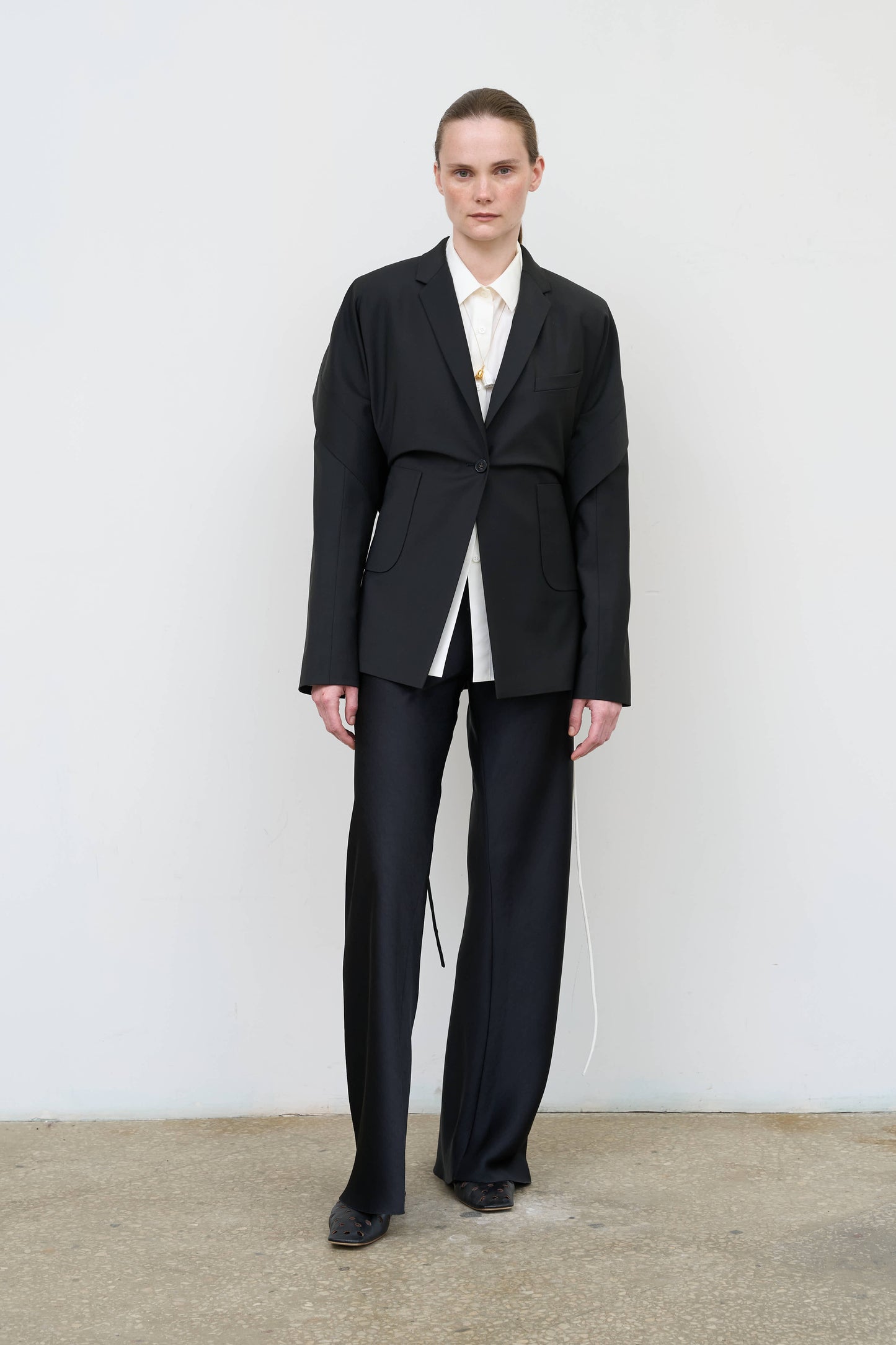 Model is wearing a black tailored wool-blend jacket by Litkovska with capelet overlay and architectural design, designer women’s jacket available at House of Woven Stories