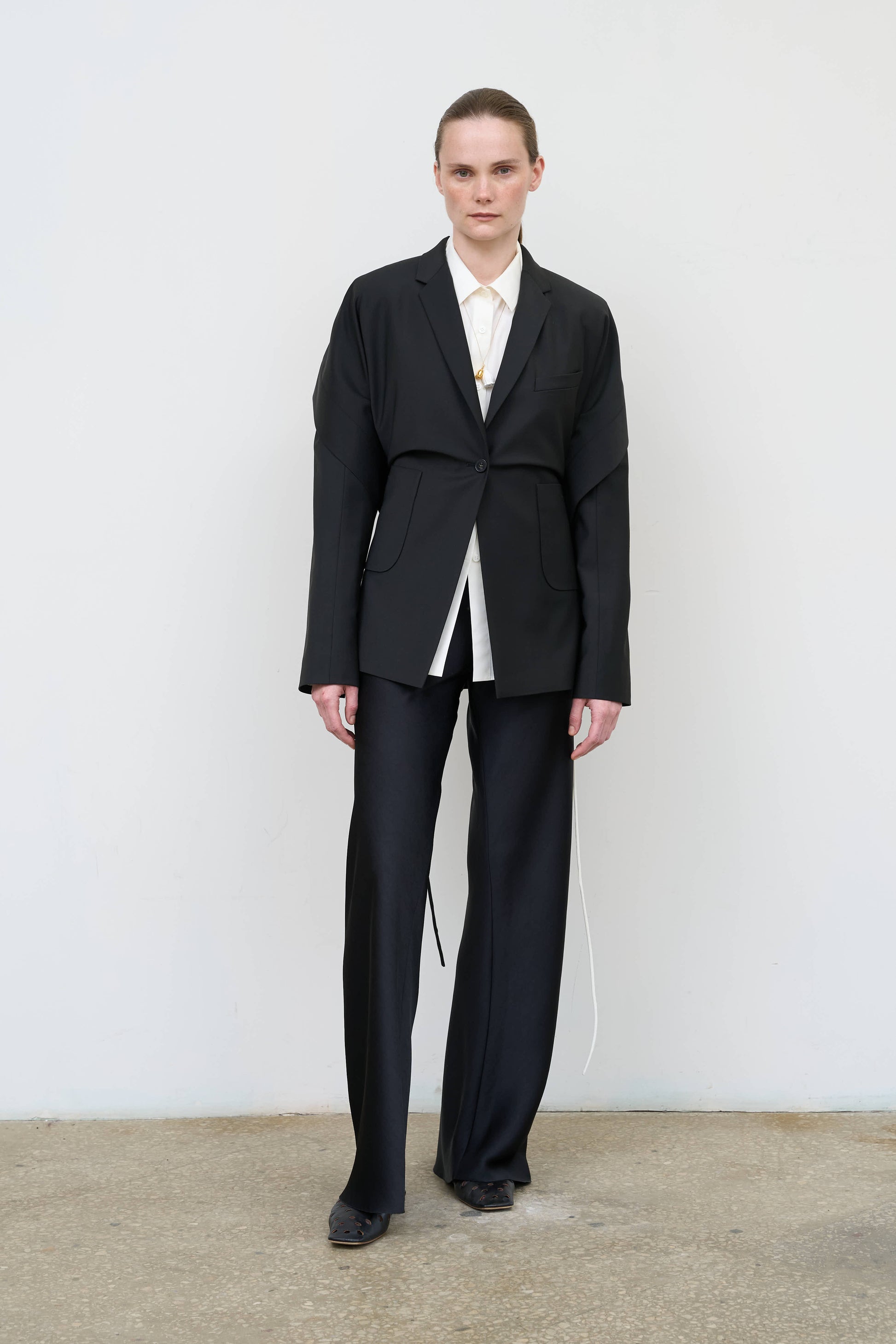 Model is wearing a black tailored wool-blend jacket by Litkovska with capelet overlay and architectural design, designer women’s jacket available at House of Woven Stories