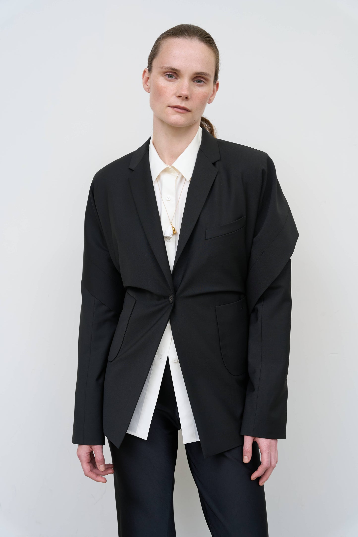 Model is wearing a black tailored wool-blend jacket by Litkovska with capelet overlay and architectural design, designer women’s jacket available at House of Woven Stories
