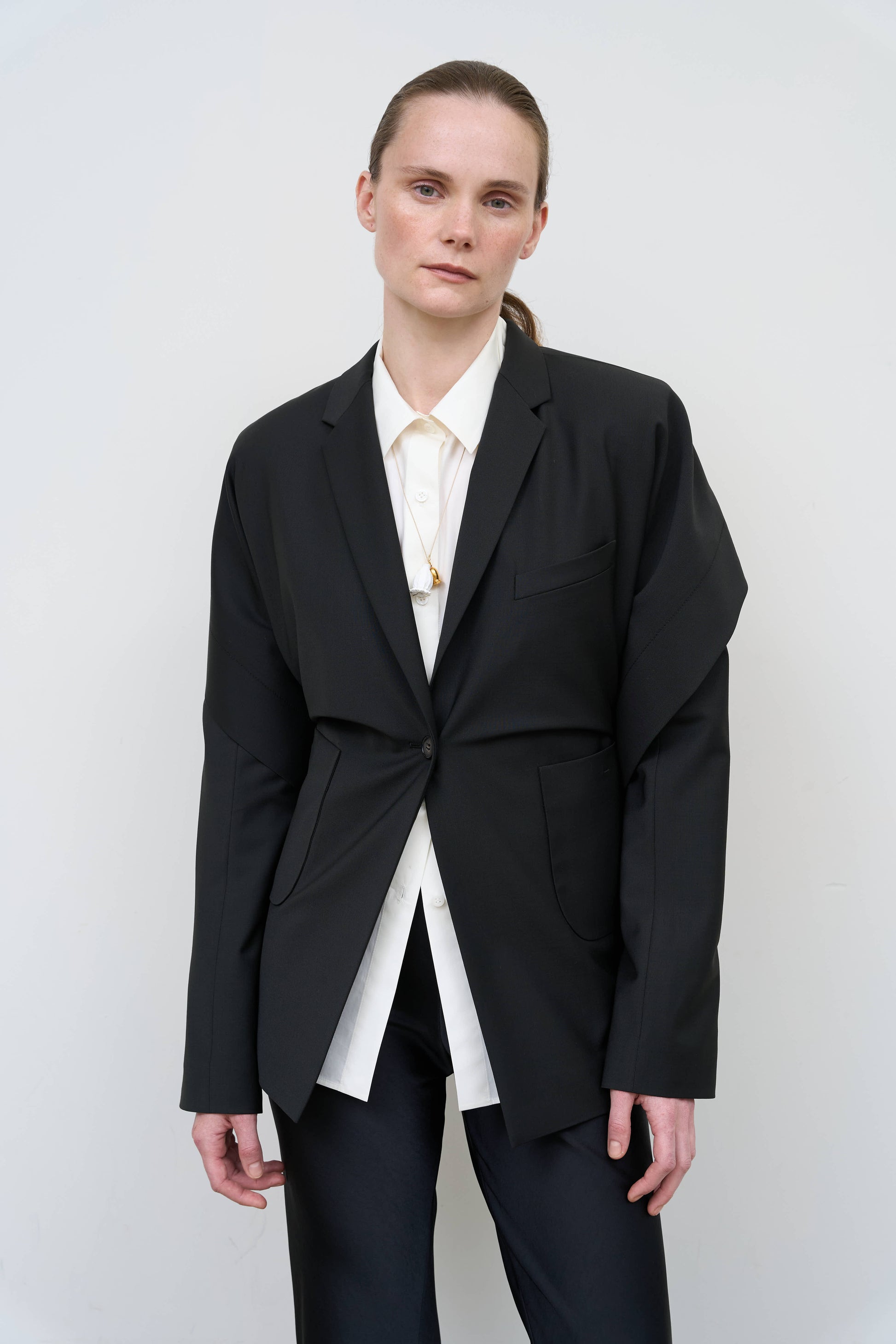 Model is wearing a black tailored wool-blend jacket by Litkovska with capelet overlay and architectural design, designer women’s jacket available at House of Woven Stories
