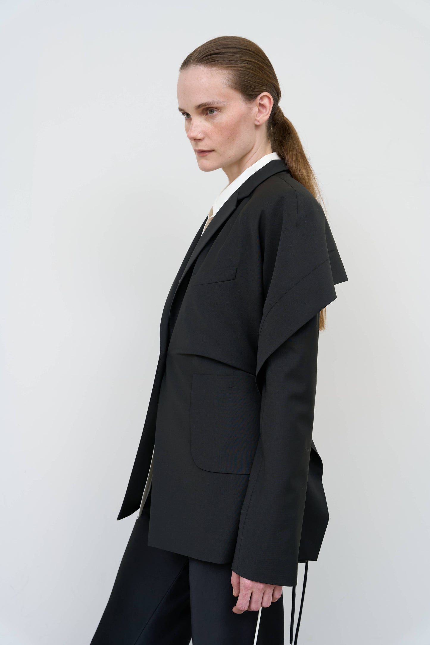 Model is wearing a black tailored wool-blend jacket by Litkovska with capelet overlay and architectural design, designer women’s jacket available at House of Woven Stories