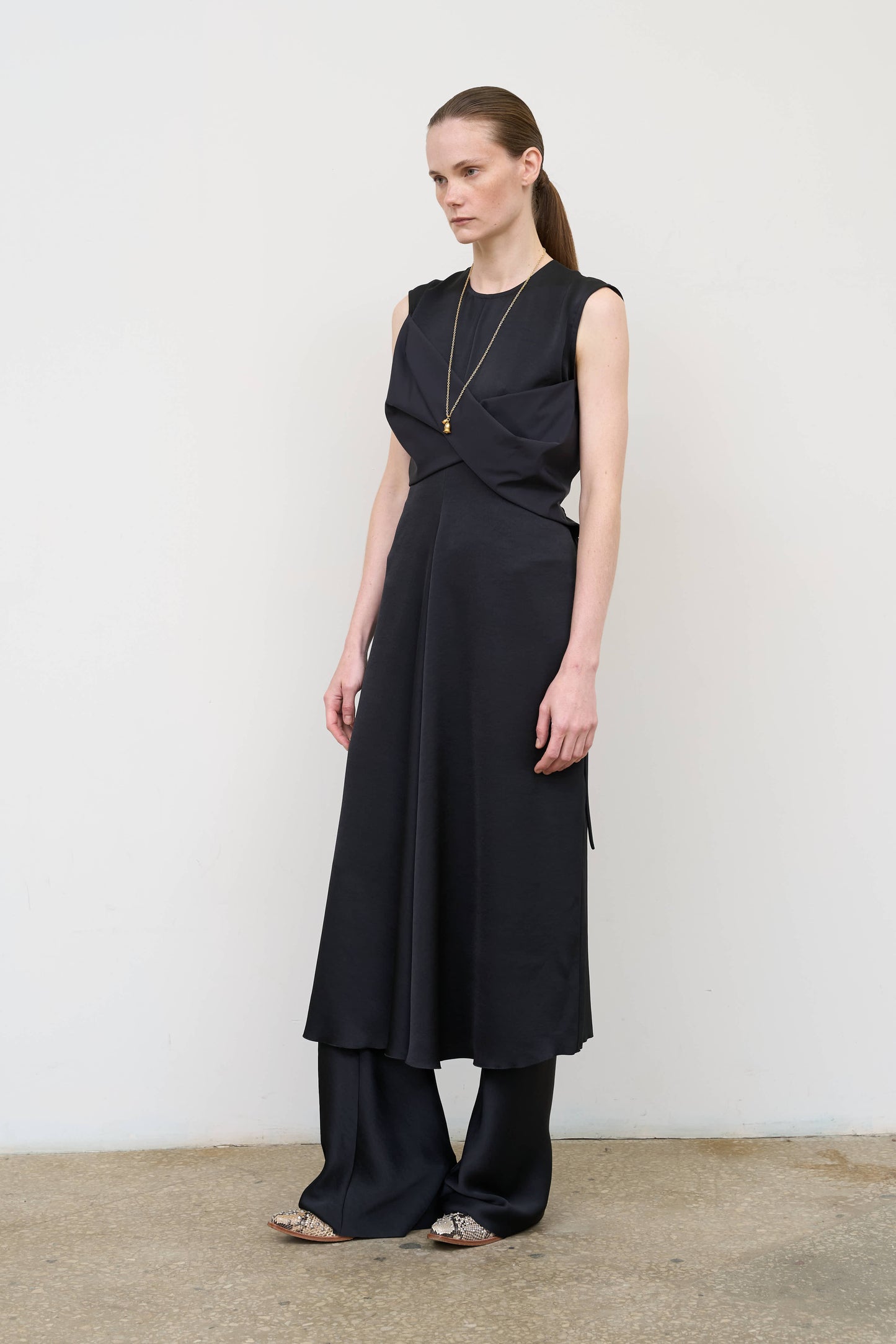 Model is wearing a black waist-twisted satin dress by Litkovska with sculptural twist at the waist and fluid silhouette, designer women’s dress available at House of Woven Stories