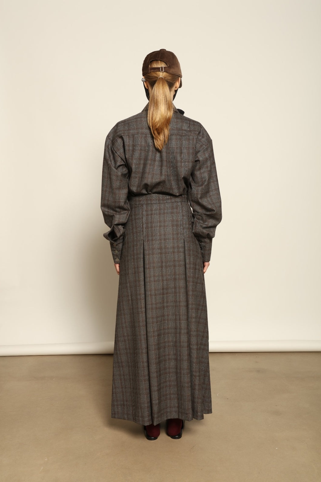Model is wearing the Londra Brown Checked Skirt by House of Woven Stories, ankle-length with fine pleats and brown checked pattern, combining timeless tailoring with contemporary elegance and quality craftsmanship.