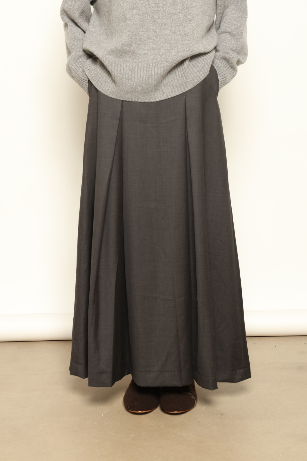 Model is wearing the Londra Grey Merino Wool Skirt by House of Woven Stories – crafted in Italy with subtle pleats, a flattering structured silhouette, and soft grey tones for timeless elegance.