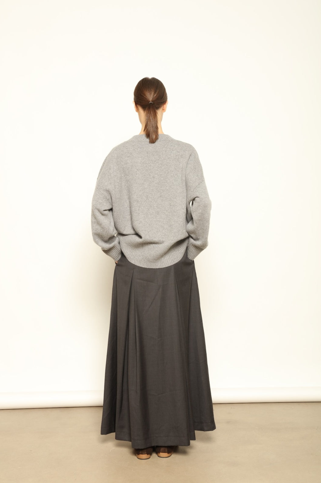 Model is wearing the Londra Grey Merino Wool Skirt by House of Woven Stories – crafted in Italy with subtle pleats, a flattering structured silhouette, and soft grey tones for timeless elegance.