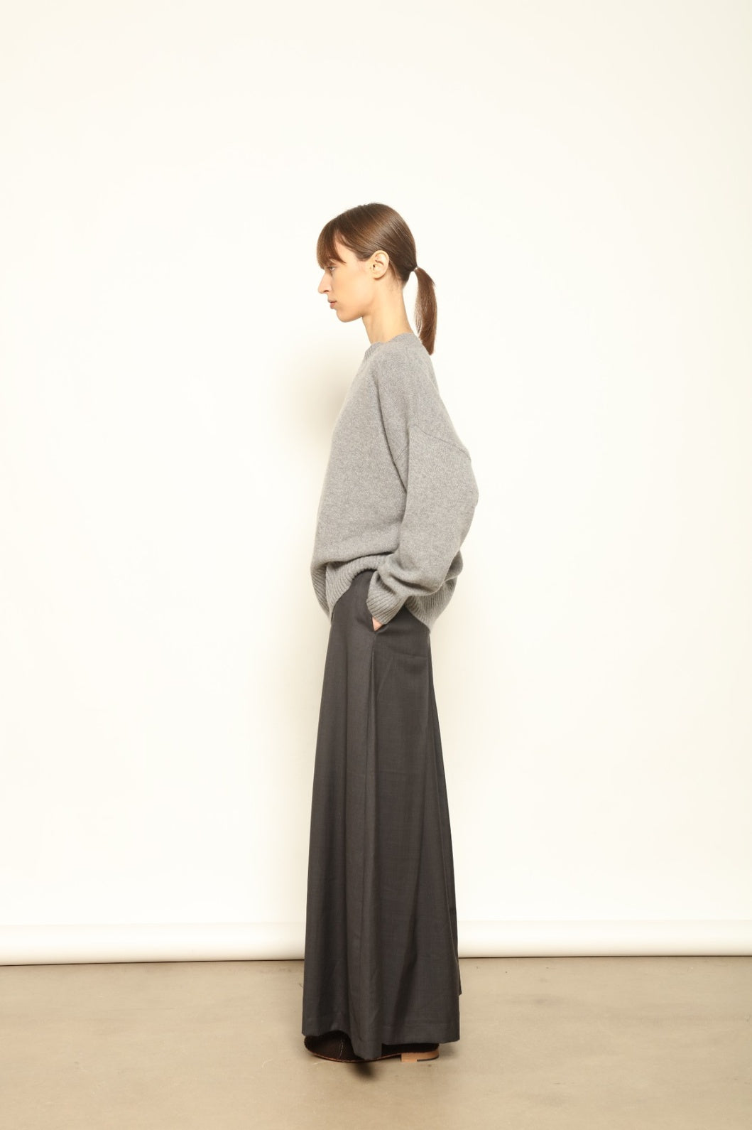 Model is wearing the Londra Grey Merino Wool Skirt by House of Woven Stories – crafted in Italy with subtle pleats, a flattering structured silhouette, and soft grey tones for timeless elegance.