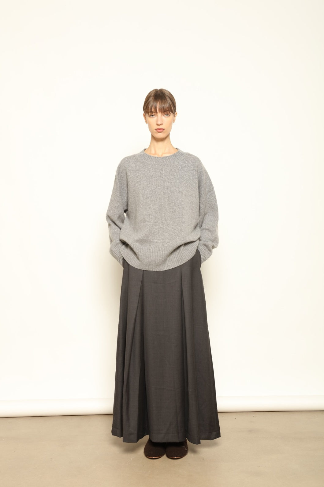 Model is wearing the Londra Grey Merino Wool Skirt by House of Woven Stories – crafted in Italy with subtle pleats, a flattering structured silhouette, and soft grey tones for timeless elegance.