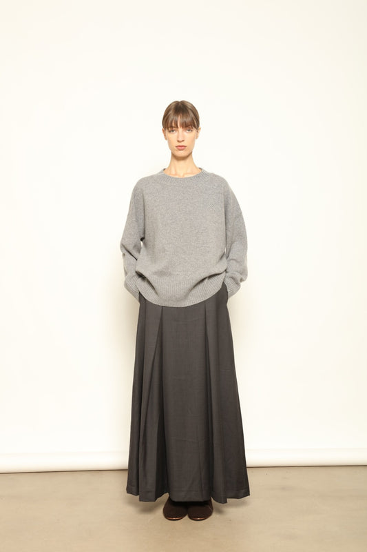 Model is wearing the Londra Grey Merino Wool Skirt by House of Woven Stories – crafted in Italy with subtle pleats, a flattering structured silhouette, and soft grey tones for timeless elegance.