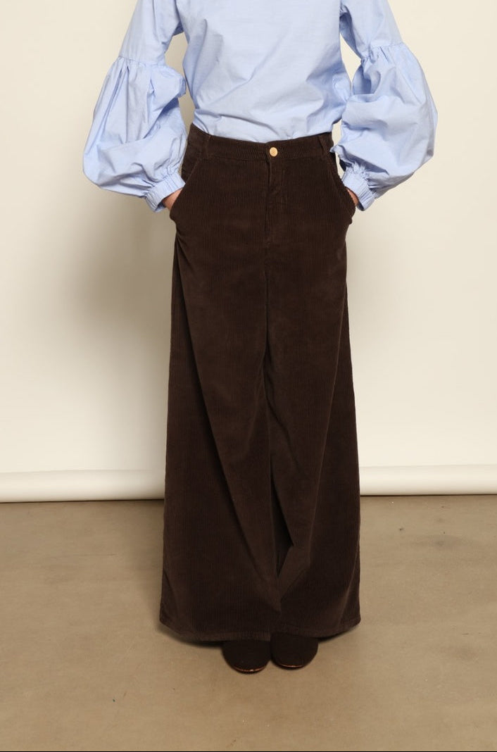 Model is wearing the Maron Foncè Le Pantalon Over Chino by Happy Haus, crafted in soft velour with a wide flowing silhouette, removable belt, back embroidered peacock, and wooden button detail for versatile, relaxed-chic style.