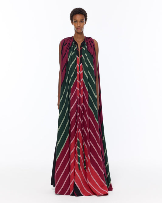 Model is wearing the Cape Dress by Marrakshi Life, a hand-woven striped dress in green and red with adjustable neckline ties and a flowing cape-like silhouette, curated in the House of Woven Stories selection.