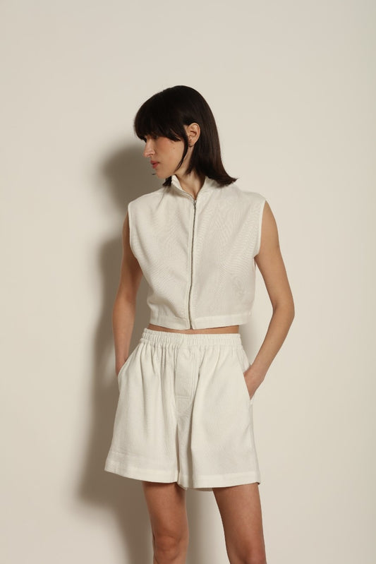 Model is wearing Marrakshi Life cropped turtleneck in white hand-loomed cotton, boxy fit high neck cropped top with minimalist design styled with high-waisted trousers