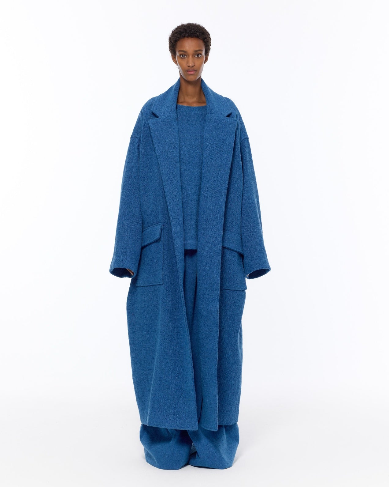 Model is wearing the French Blue Bouclé Blanket Coat by Marrakshi Life, a hand-woven oversized cotton bouclé coat with a deep shawl collar and textured finish, curated in the House of Woven Stories selection.