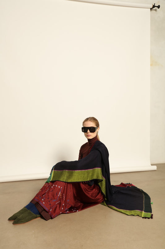Model is wearing the Miraj 142 Cashmere Scarf by Injiri, handwoven from Himalayan cashmere with a dark base and rich indigo, turquoise, purple, brown, and green borders, combining warmth, softness, and artisanal elegance.