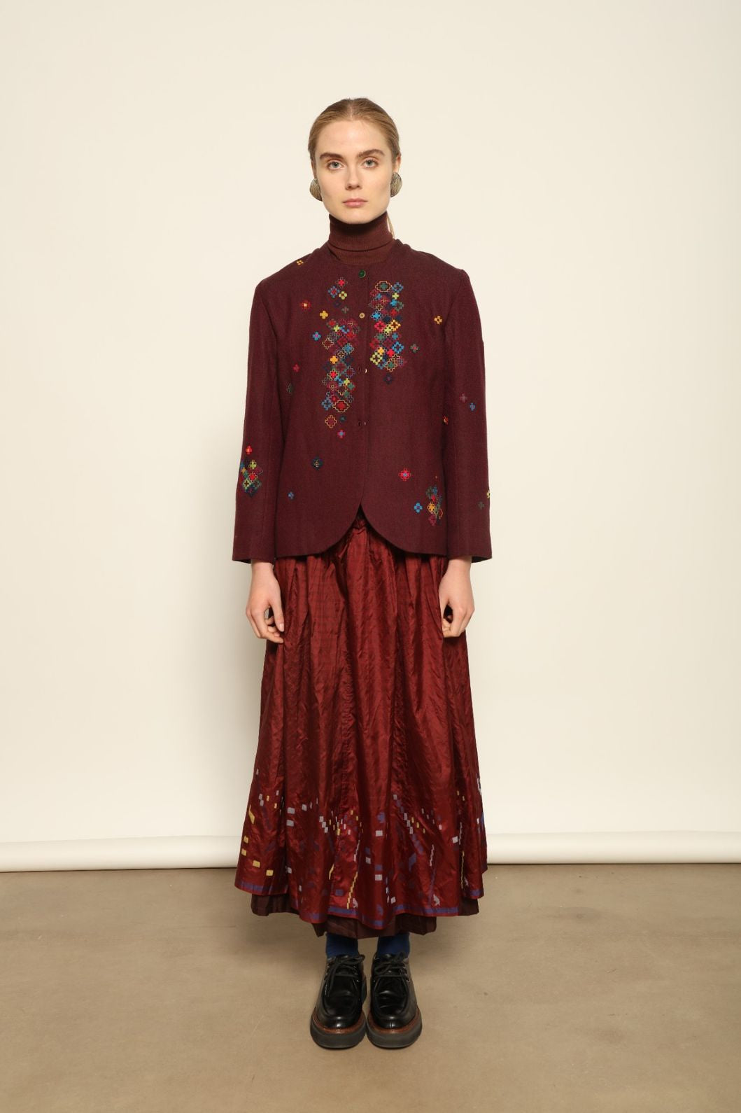 Model is wearing the Miraj 103 Silk Skirt by Injiri, handcrafted in red silk with vibrant rectangular motifs along the hem, blending artistry, movement, and refined elegance.