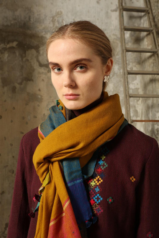 Model is wearing the Miraj 140 Cashmere Scarf by Injiri, handwoven from Kashmir cashmere with a vibrant ochre base and multicolor block borders, blending warmth, softness, and artisanal craftsmanship.