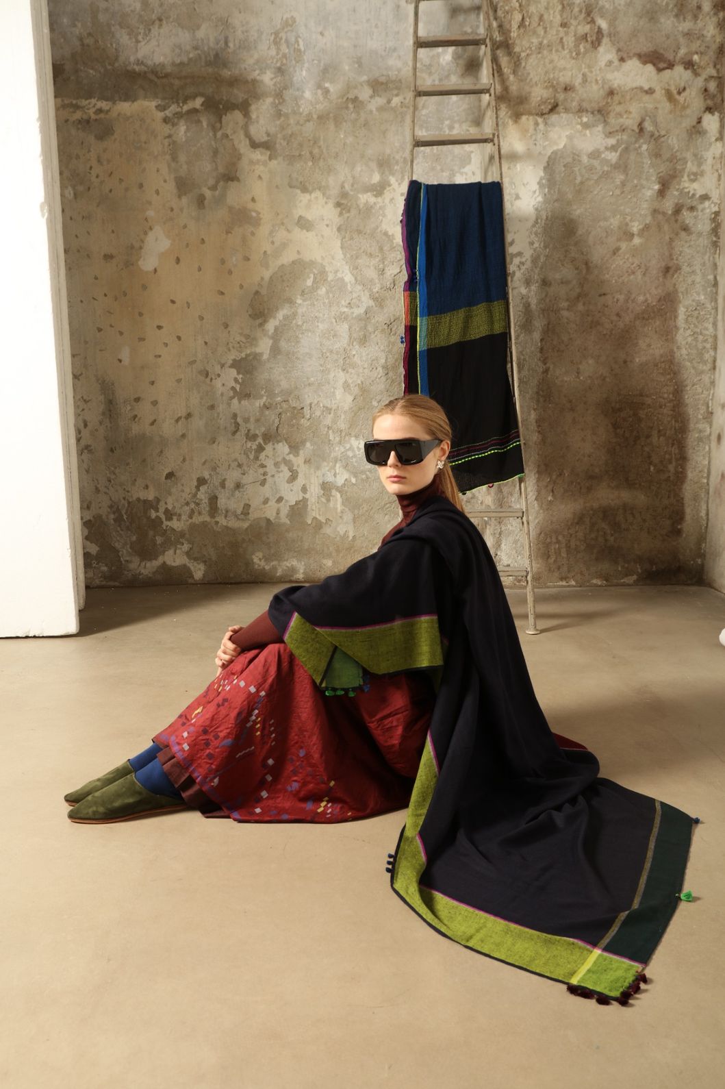 Model is wearing the Miraj 142 Cashmere Scarf by Injiri, handwoven from Himalayan cashmere with a dark base and rich indigo, turquoise, purple, brown, and green borders, combining warmth, softness, and artisanal elegance.