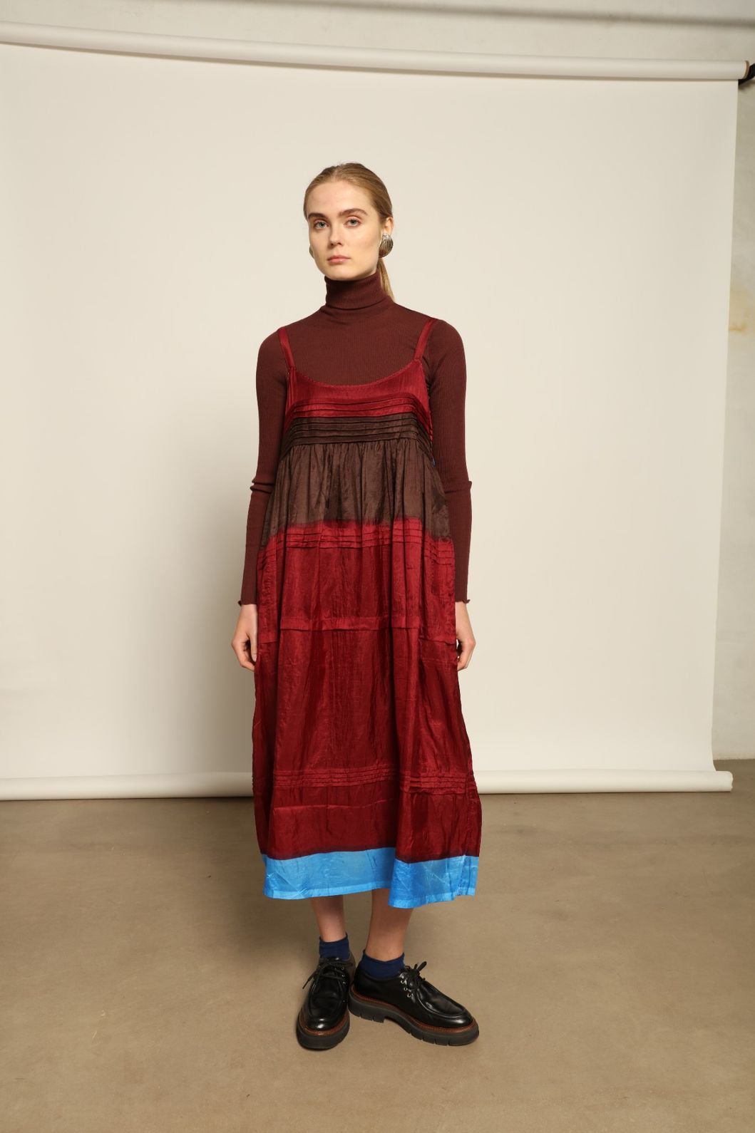 Model is wearing the Miraj 95 Silk and Cotton Slip Dress by Injiri, crafted in red and brown cotton with silk accents and a bold blue border, combining lightness, color, and refined craftsmanship.
