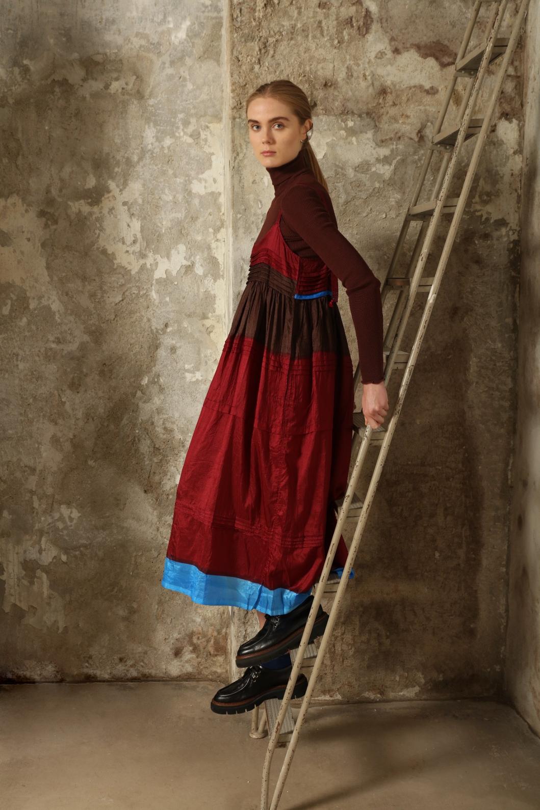 Model is wearing the Miraj 95 Silk and Cotton Slip Dress by Injiri, crafted in red and brown cotton with silk accents and a bold blue border, combining lightness, color, and refined craftsmanship.