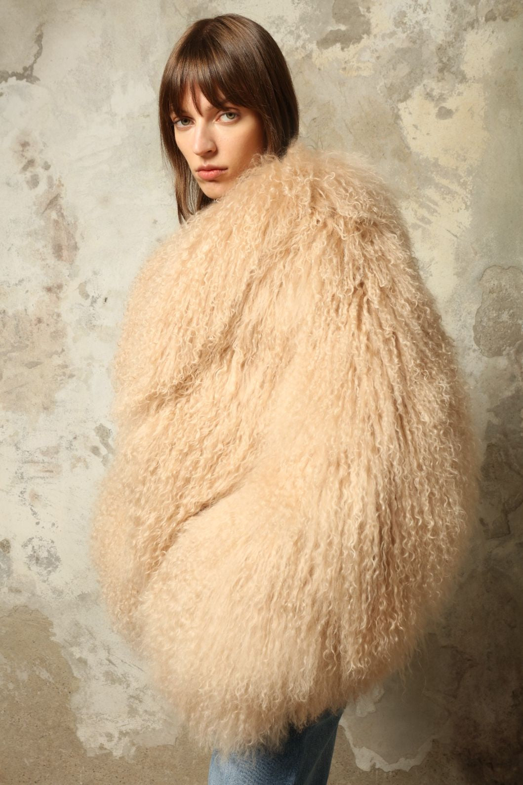 Model is wearing the Mongolia Camel Shearling Jacket by Blancha – crafted from 100% Tibetan lamb with a pure silk lining, featuring cloud-like softness, a camel hue, and expert Italian craftsmanship for a lightweight, elegant, and timeless outerwear piece.