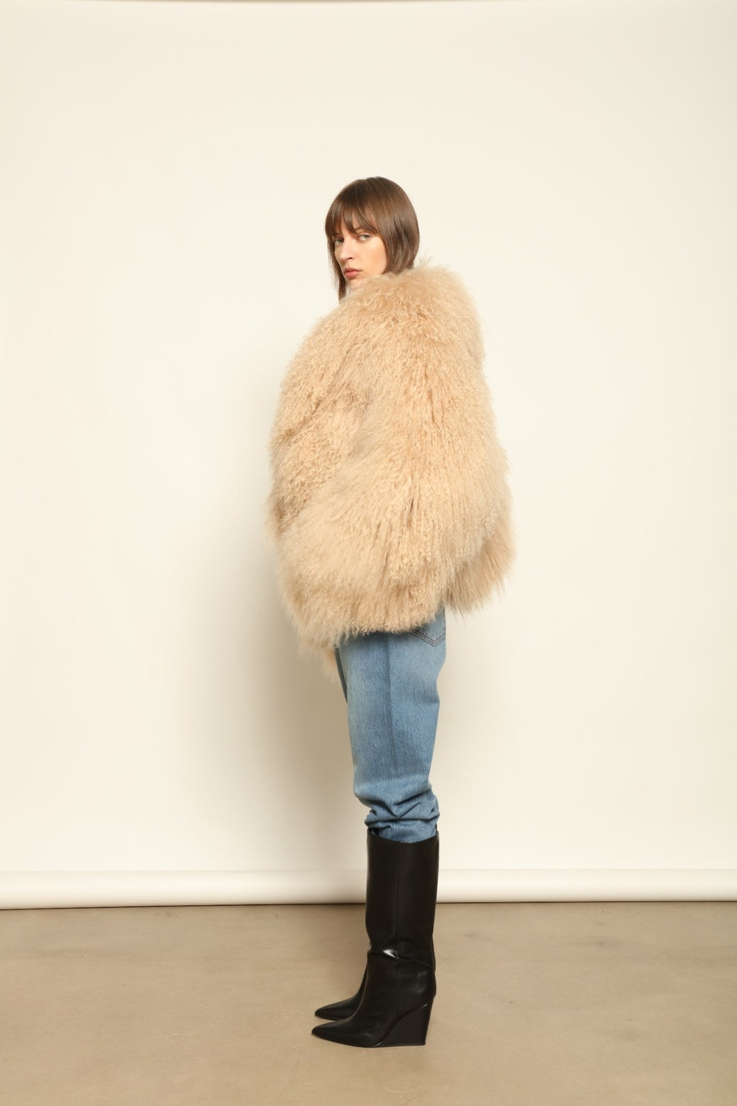 Model is wearing the Mongolia Camel Shearling Jacket by Blancha – crafted from 100% Tibetan lamb with a pure silk lining, featuring cloud-like softness, a camel hue, and expert Italian craftsmanship for a lightweight, elegant, and timeless outerwear piece.