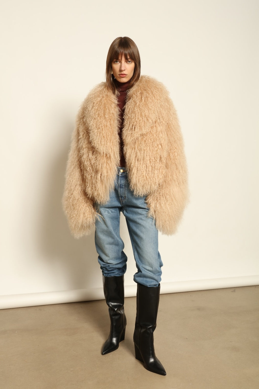 Model is wearing the Mongolia Camel Shearling Jacket by Blancha – crafted from 100% Tibetan lamb with a pure silk lining, featuring cloud-like softness, a camel hue, and expert Italian craftsmanship for a lightweight, elegant, and timeless outerwear piece.