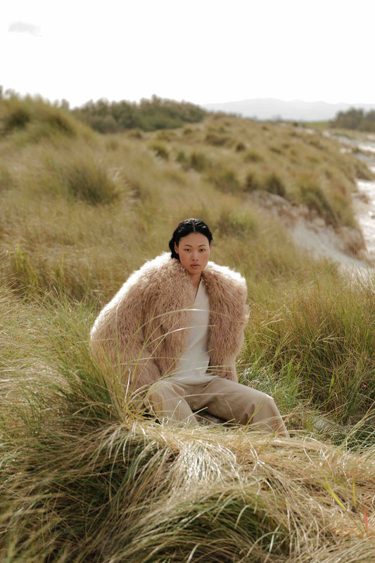 Model is wearing the Mongolia Camel Shearling Jacket by Blancha, part of the House of Woven Stories selection, crafted from 100% Tibet lamb with silk lining, featuring soft, voluminous texture and warm camel tone.