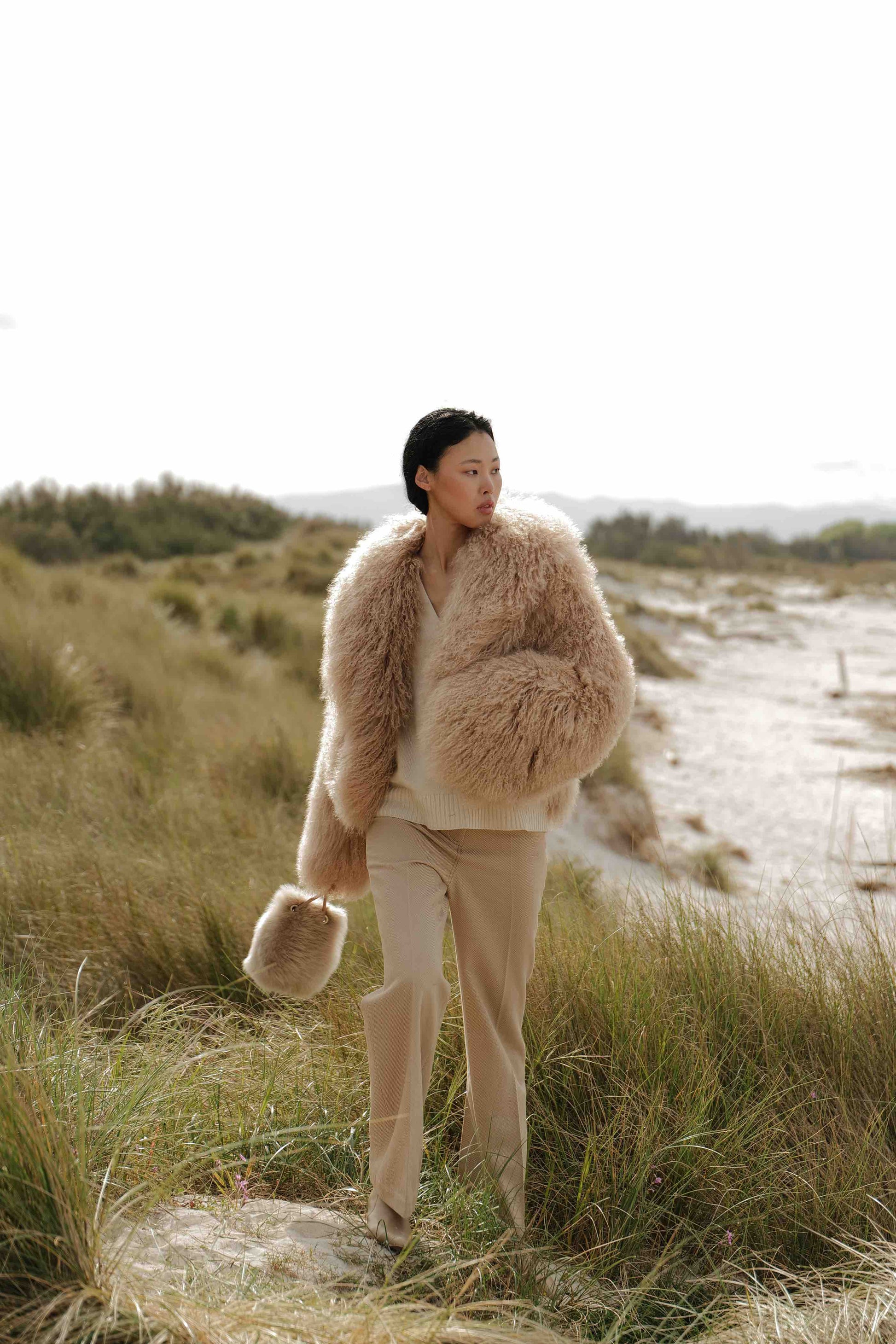 Model is wearing the Mongolia Camel Shearling Jacket by Blancha, part of the House of Woven Stories selection, crafted from 100% Tibet lamb with silk lining, featuring soft, voluminous texture and warm camel tone.