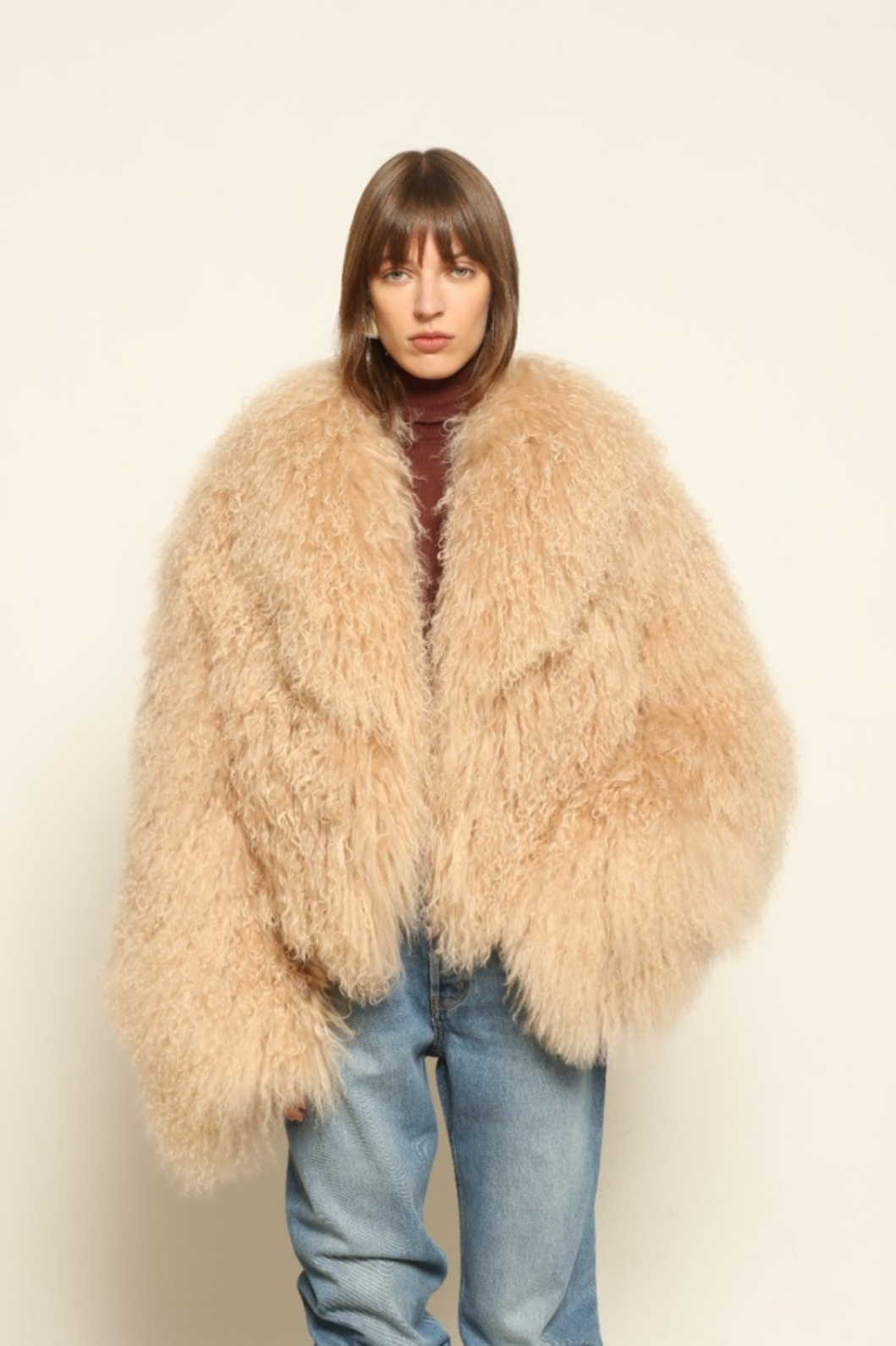 Model is wearing the Mongolia Camel Shearling Jacket by Blancha – crafted from 100% Tibetan lamb with a pure silk lining, featuring cloud-like softness, a camel hue, and expert Italian craftsmanship for a lightweight, elegant, and timeless outerwear piece.