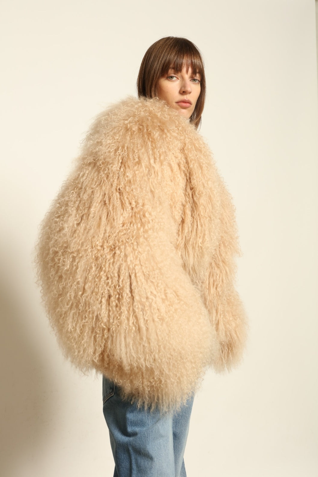 Model is wearing the Mongolia Camel Shearling Jacket by Blancha – crafted from 100% Tibetan lamb with a pure silk lining, featuring cloud-like softness, a camel hue, and expert Italian craftsmanship for a lightweight, elegant, and timeless outerwear piece.