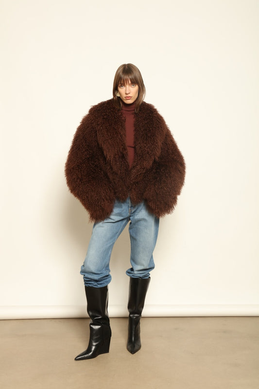 Model is wearing the Mongolia Chocolate Shearling Jacket by Blancha – crafted from 100% Tibetan lamb with pure silk lining, featuring a soft voluminous texture, deep chocolate hue, and luxurious Italian craftsmanship for feather-light warmth and timeless elegance.