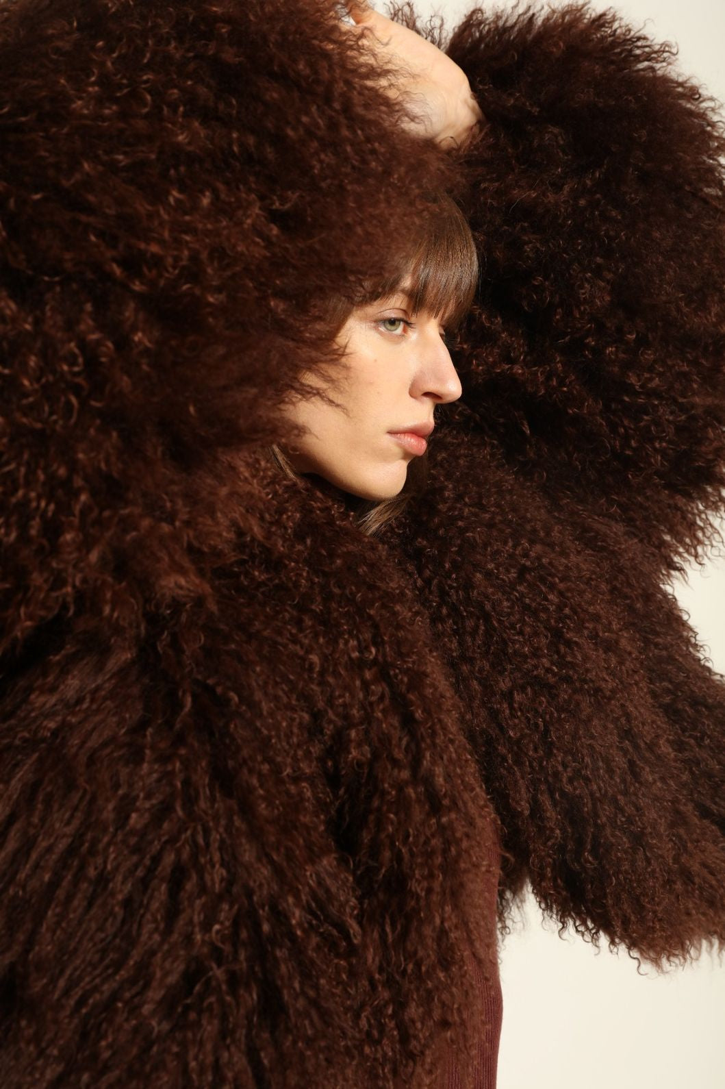 Model is wearing the Mongolia Chocolate Shearling Jacket by Blancha – crafted from 100% Tibetan lamb with pure silk lining, featuring a soft voluminous texture, deep chocolate hue, and luxurious Italian craftsmanship for feather-light warmth and timeless elegance.
