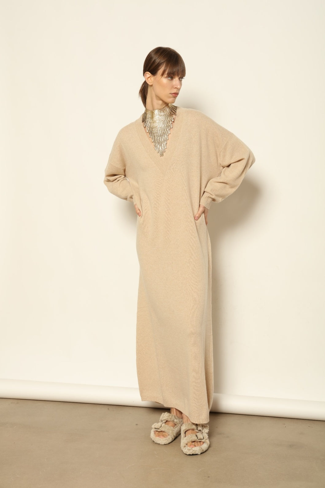 Model is wearing the Natural Katharina V-Neck Cashmere Maxi Dress by House of Woven Stories, crafted from 100% pure Inner Mongolia cashmere in its uncoloured natural shade, featuring a long flowing silhouette, soft breathable knit, elegant V-neckline, and timeless sustainable luxury design