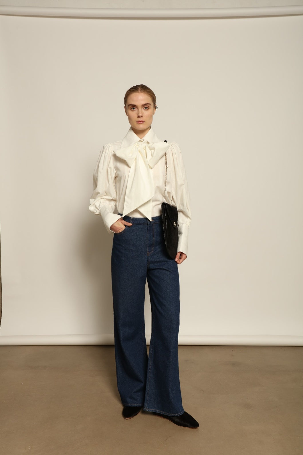 Model is wearing Le Pantalon Peacock in Brut Vintage by Happy Haus, high-waisted wide-leg cotton trousers with double-stitched back pockets and delicate embroidered peacock detail, combining timeless elegance with relaxed sophistication.