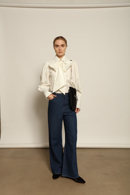 Model is wearing Le Pantalon Peacock in Brut Vintage by Happy Haus, high-waisted wide-leg cotton trousers with double-stitched back pockets and delicate embroidered peacock detail, combining timeless elegance with relaxed sophistication.