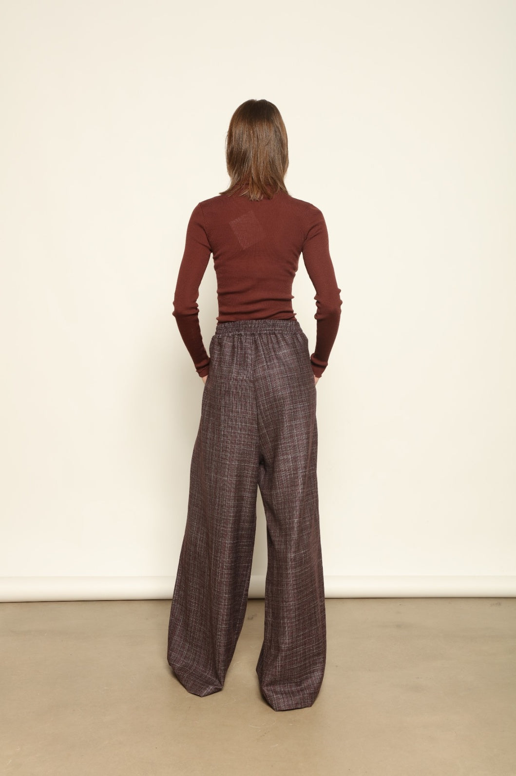 Model is wearing the Parigi Burgundy Lana Trousers by House of Woven Stories – Italian-tailored trousers crafted from a luxurious blend of merino wool, silk, and linen, featuring front pleats, side pockets, and a relaxed yet elegant burgundy silhouette.