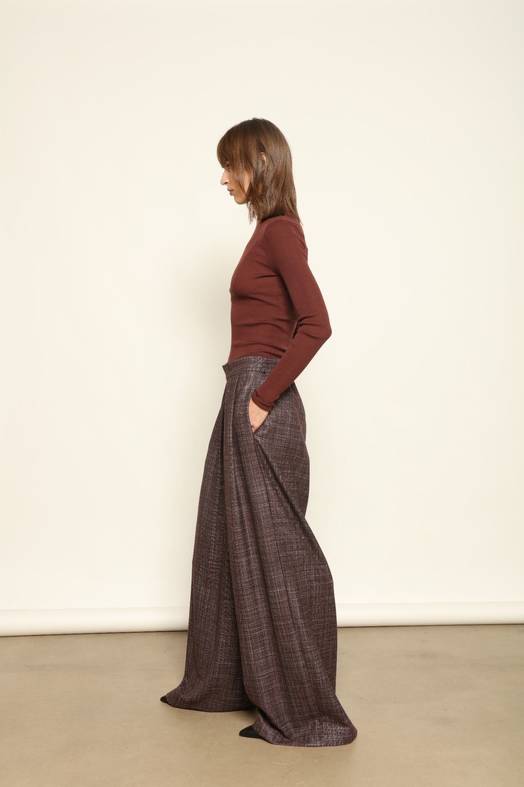 Model is wearing the Parigi Burgundy Lana Trousers by House of Woven Stories – Italian-tailored trousers crafted from a luxurious blend of merino wool, silk, and linen, featuring front pleats, side pockets, and a relaxed yet elegant burgundy silhouette.