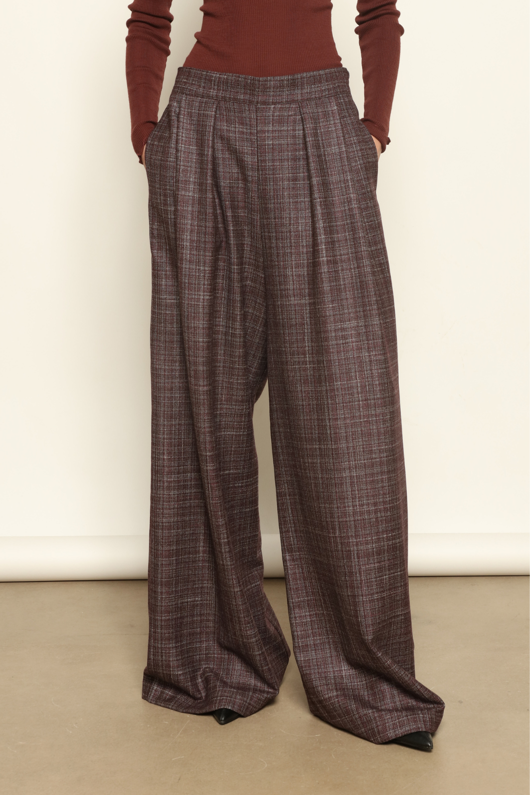 Model is wearing the Parigi Burgundy Lana Trousers by House of Woven Stories – Italian-tailored trousers crafted from a luxurious blend of merino wool, silk, and linen, featuring front pleats, side pockets, and a relaxed yet elegant burgundy silhouette.