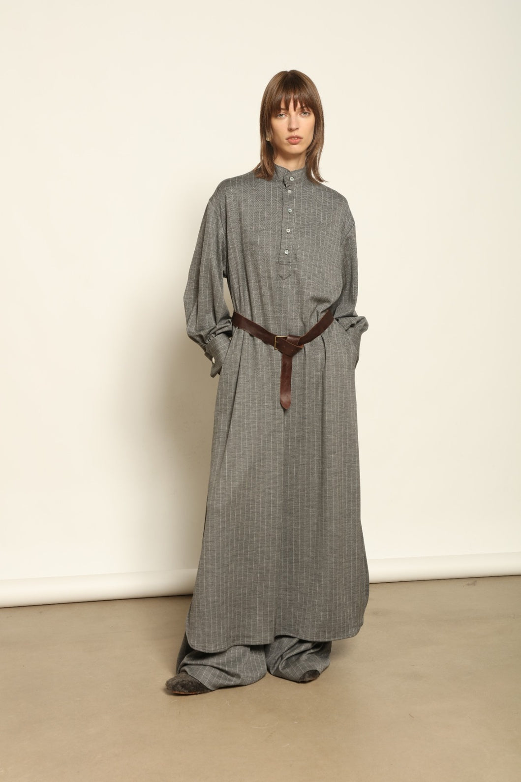 Model is wearing the Paul Dress by House of Woven Stories, made from sustainable wool with vertical stripes, a stand collar, and versatile styling for effortless elegance.